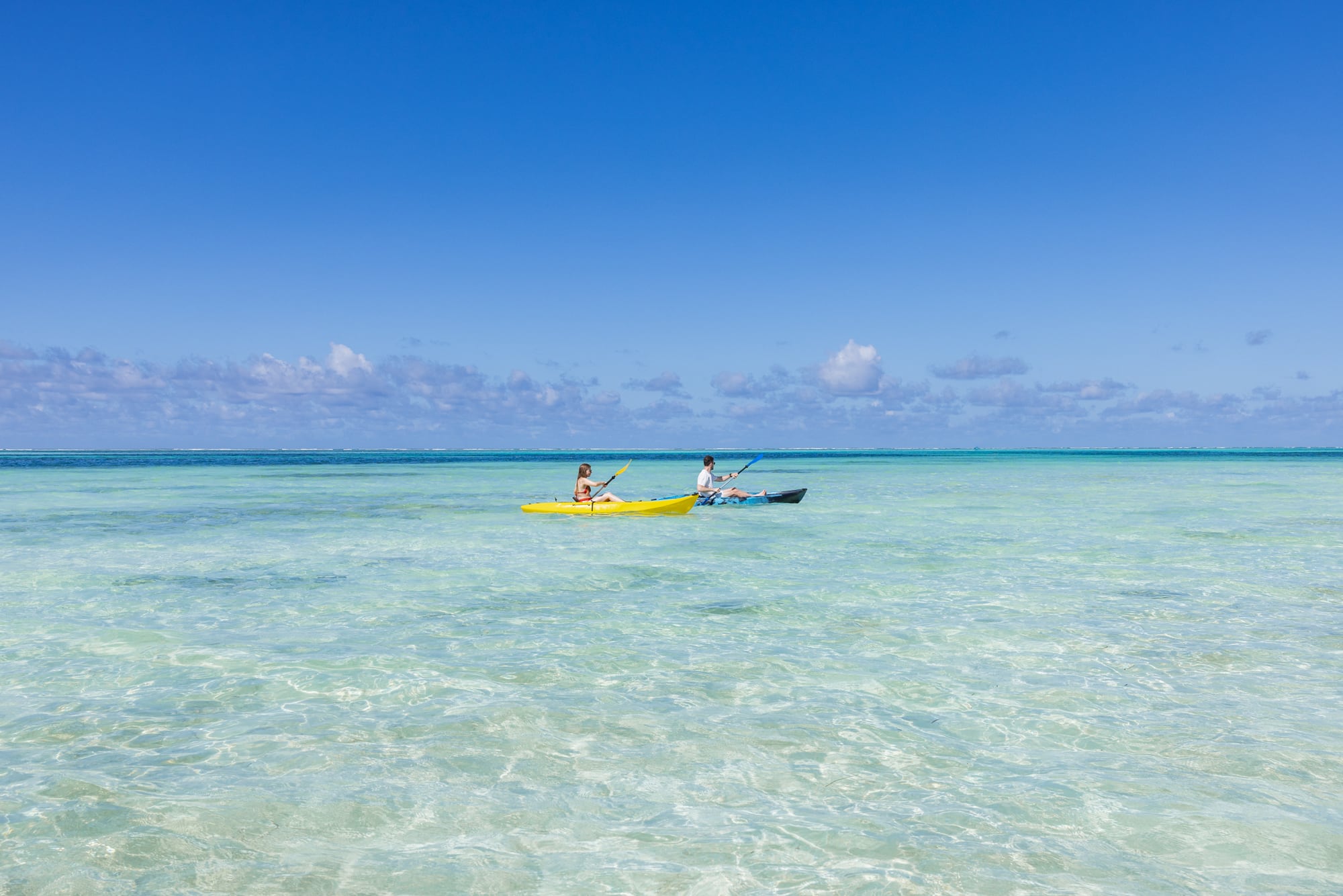 Two guests paddling kayaks over the shallow water in front of the hotel.