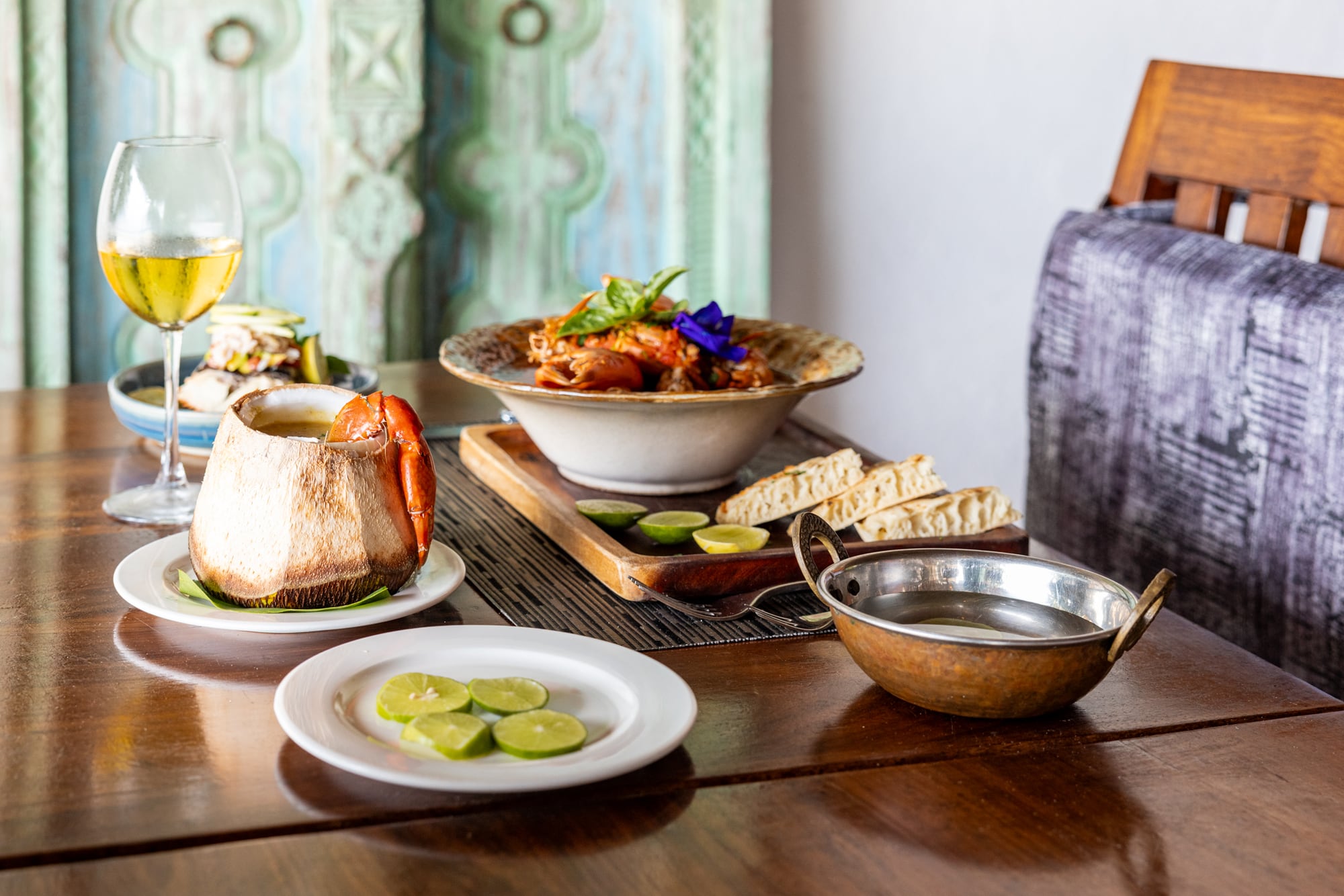 A seafood plate served in a coconut shell at Zatiny, with lime and wine on a wooden table.