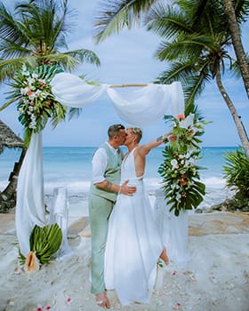 couple kissing under wedding arch during beach wedding in Zanzibar with palm trees and ocean view