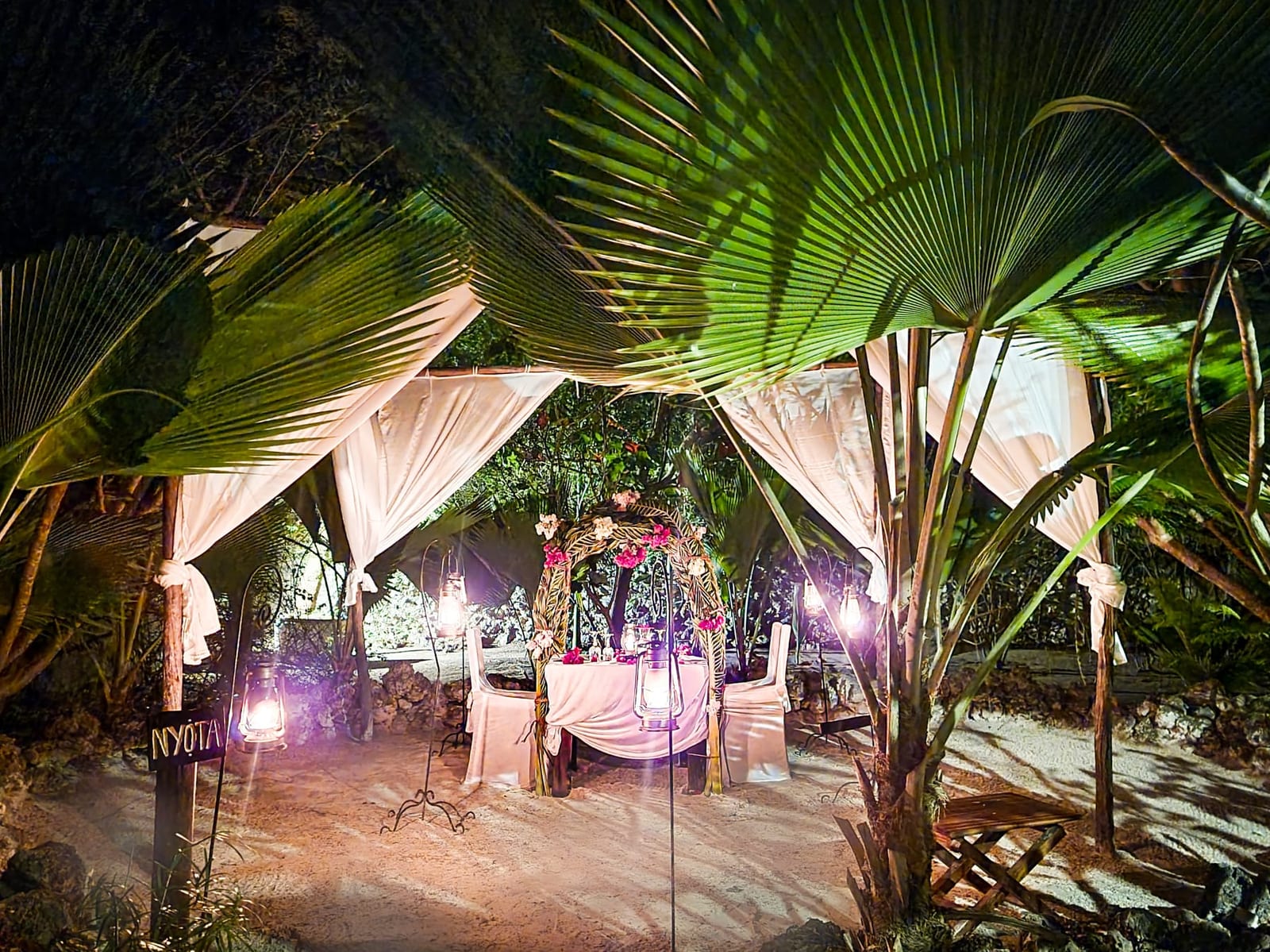 Candlelit dinner setting with lanterns on the beach at night
