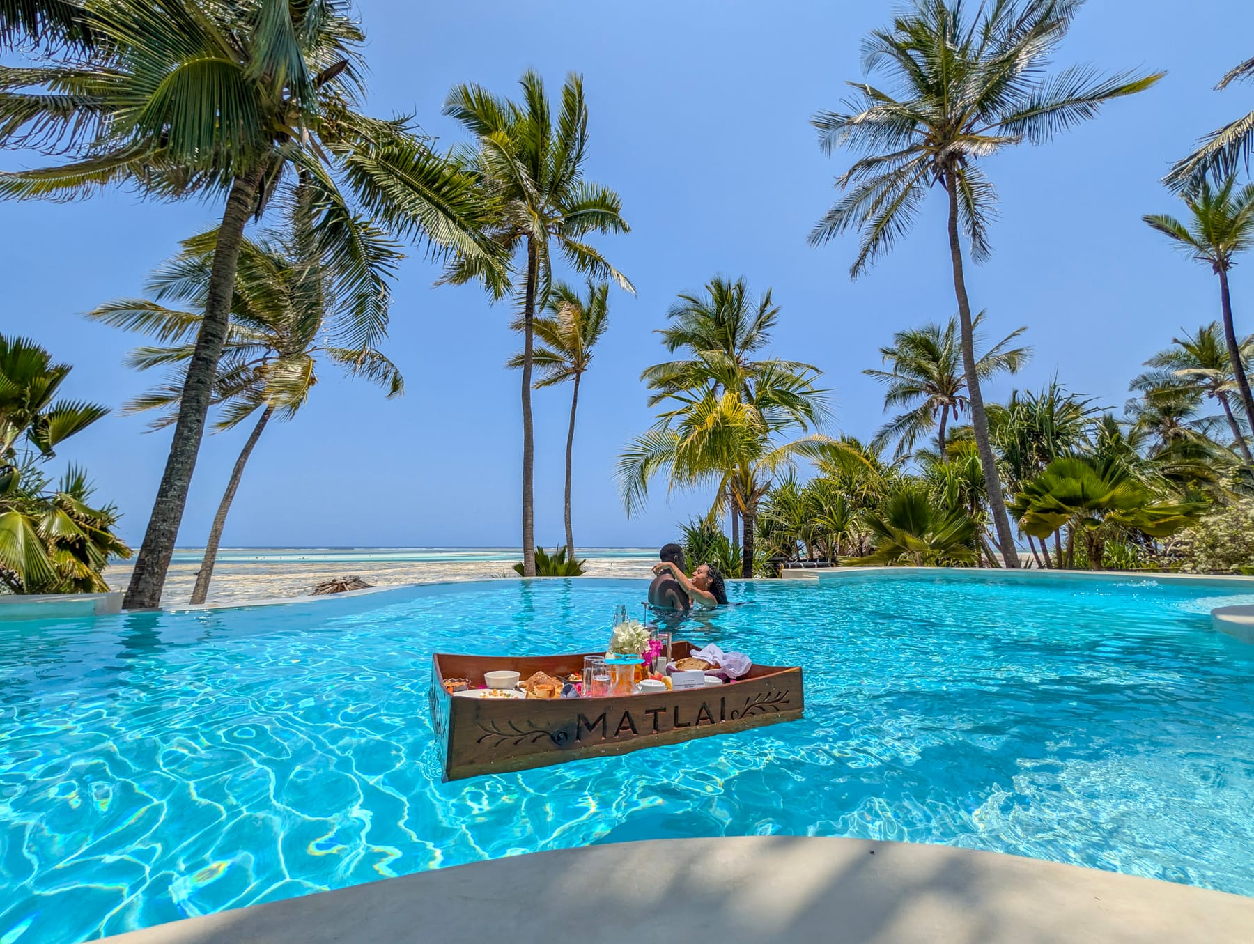 A floating breakfast tray in the infinity pool with palms and the ocean beyond