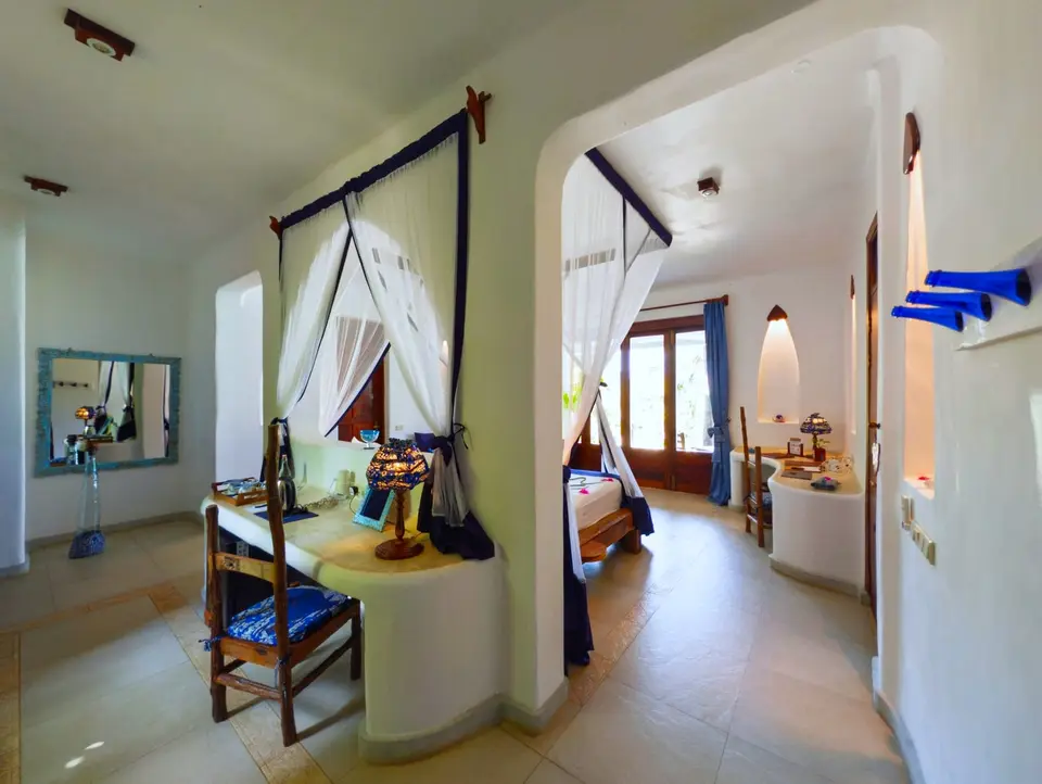 Innenansicht von Zimmer Maji im Asili House, Boutique Hotel Matlai Sansibar, mit handgefertigter Deko, darunter Tuchhalter aus blauen Flaschen und Kerzen aus recyceltem Öl.