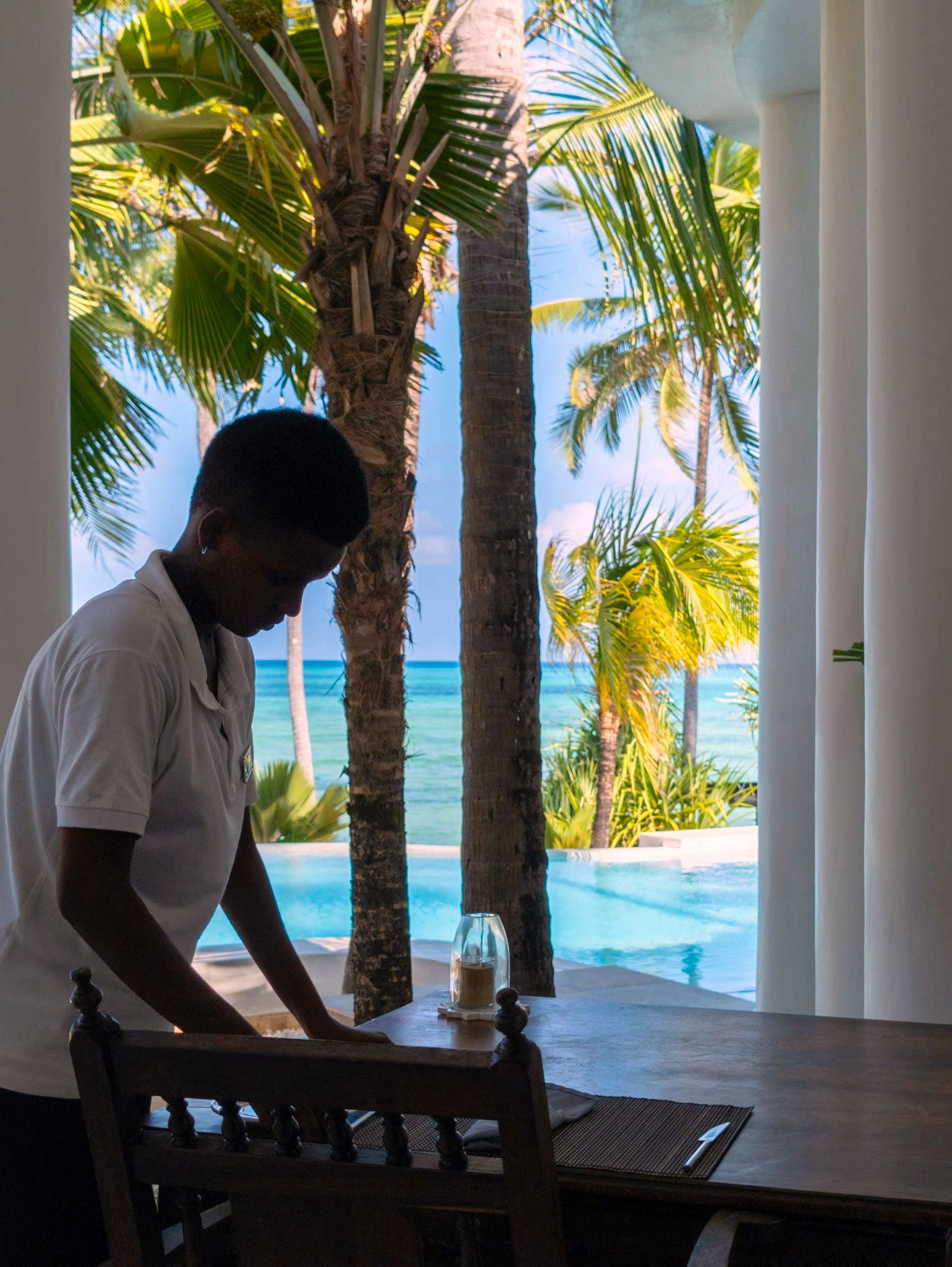 A member of staff laying a table beside the pool at Villa Kidosho, the ocean behind