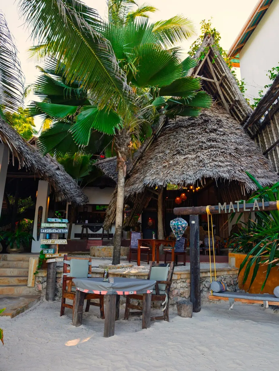 Eingang zur Beach Bar im Boutique Hotel Matlai Sansibar mit großer Schaukel und Esstisch aus einem Dhau-Boot mit Blick auf den Strand.