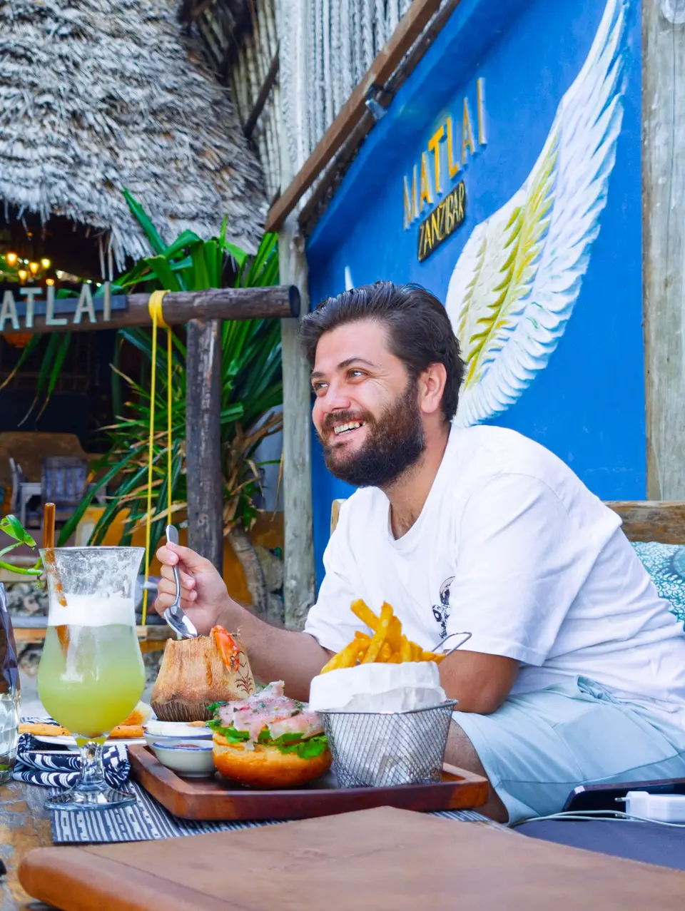 Gast sitzt auf einer Dhau-Liege am Strand des Boutique Hotel Matlai Sansibar und genießt einen Mocktail und Essen.