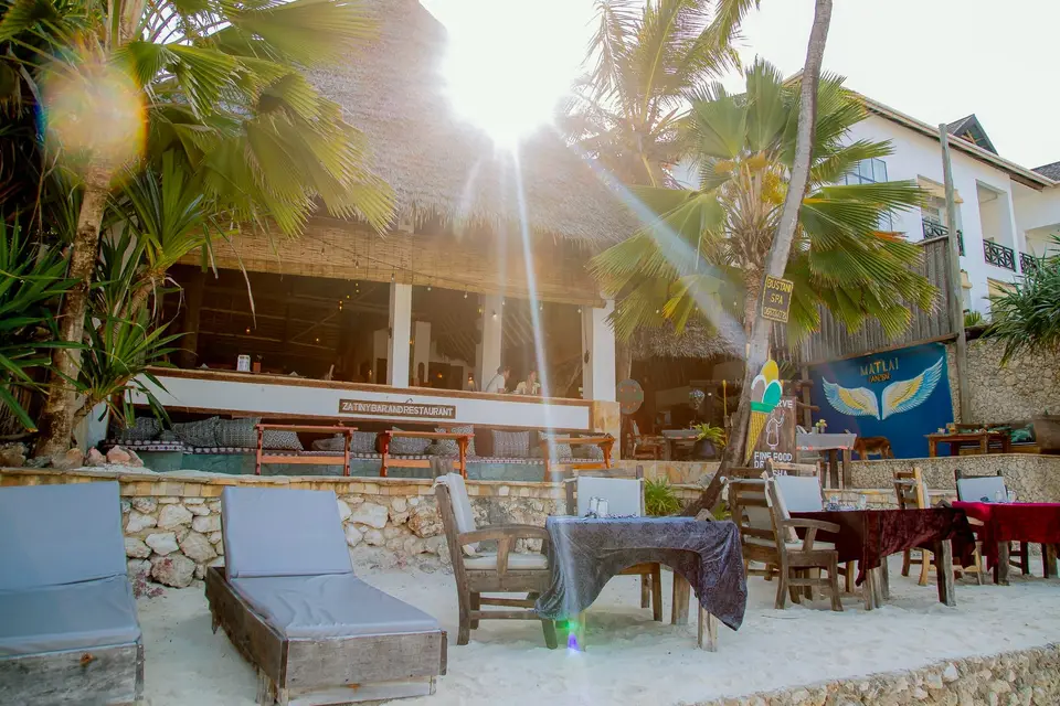 Zatiny Restaurant im Boutique Hotel Matlai Sansibar, vom Strand aus gesehen, mit Esstischen am Strand, Sonnenliegen, Baraza-Lounge und Stranddusche.