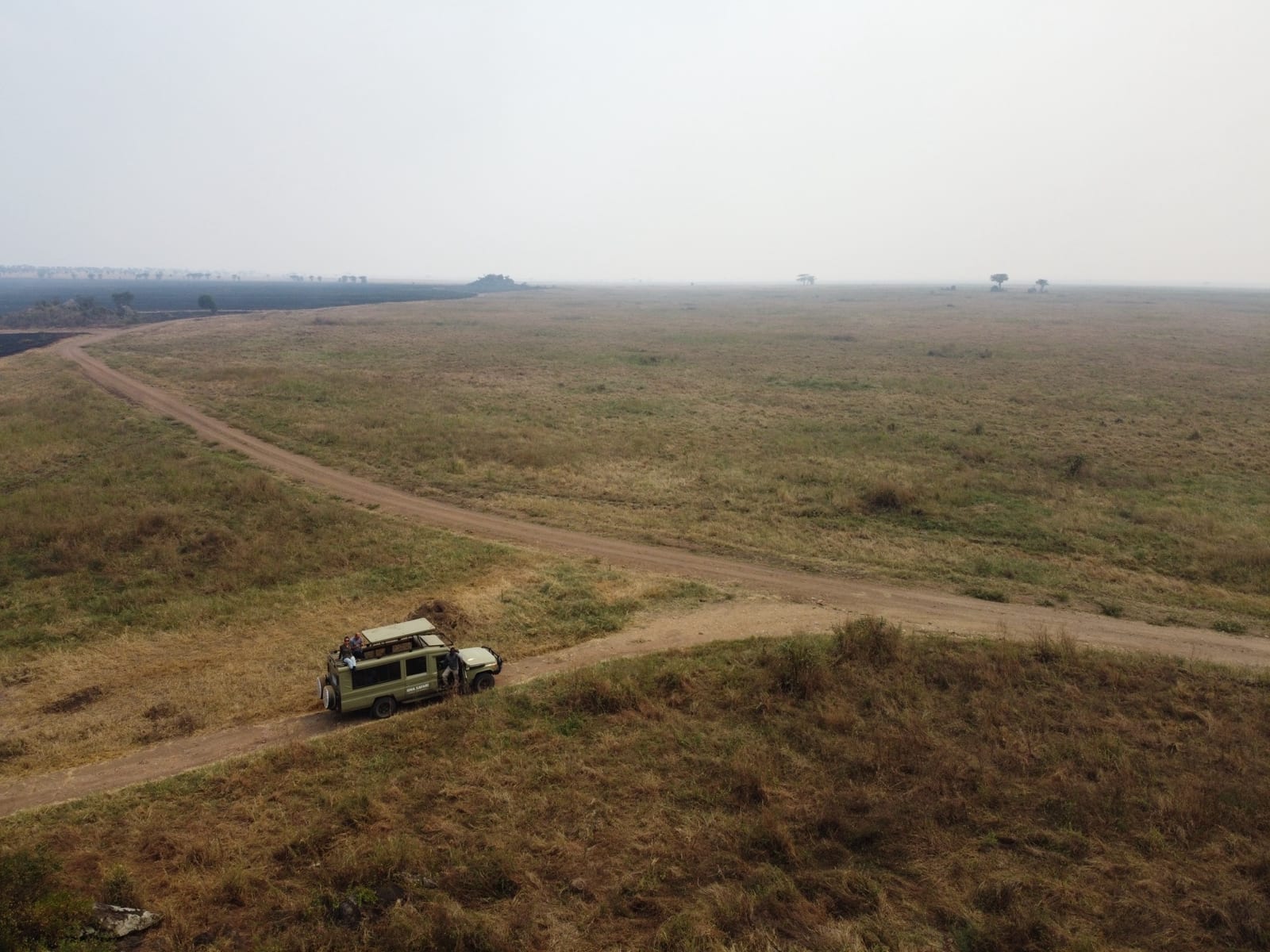 Safari vehicle on a dirt track through dry grassland