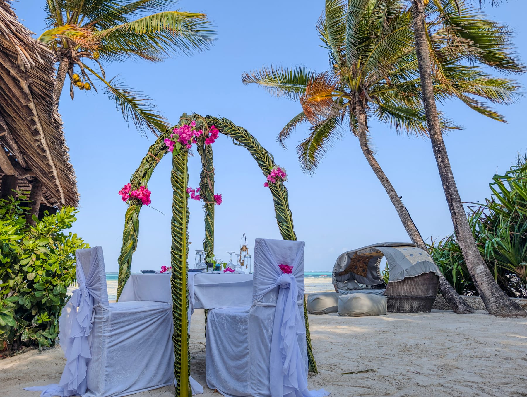 A wedding arch of woven palm and bougainvillea over a table for two on the beach